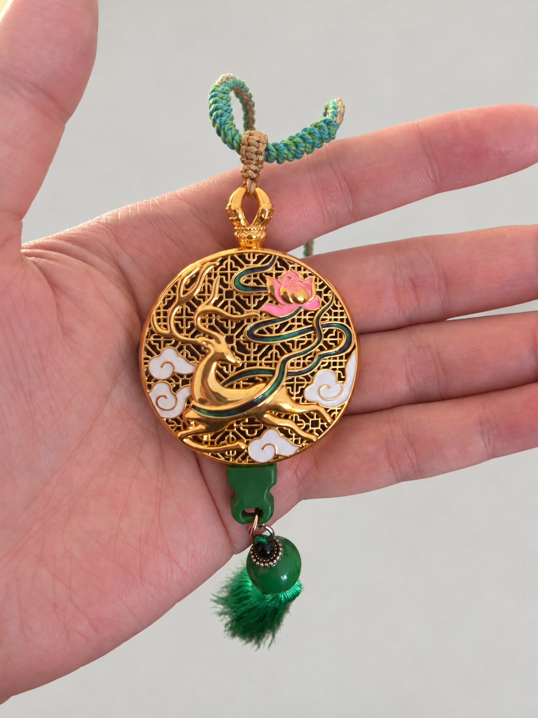 Retouched overview of the deer and lotus music pendant with a braided cord and green tassel, shown in hand.