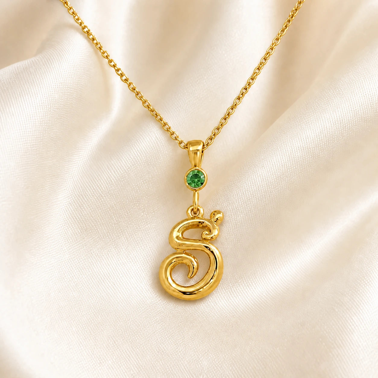 Gold S initial necklace with a green birthstone on satin