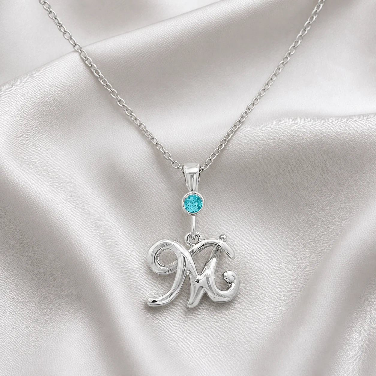 Silver M initial necklace with a blue birthstone on satin